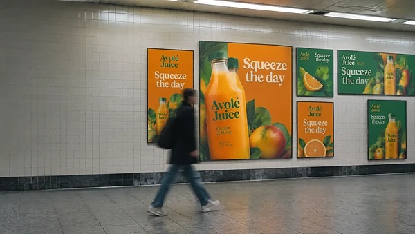 Underground passage wall covered in bold orange and green juice ads in several sizes