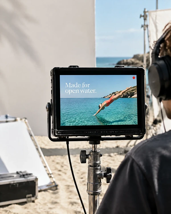 Film monitor on a beach set showing a swimmer diving in a coral swimsuit ad