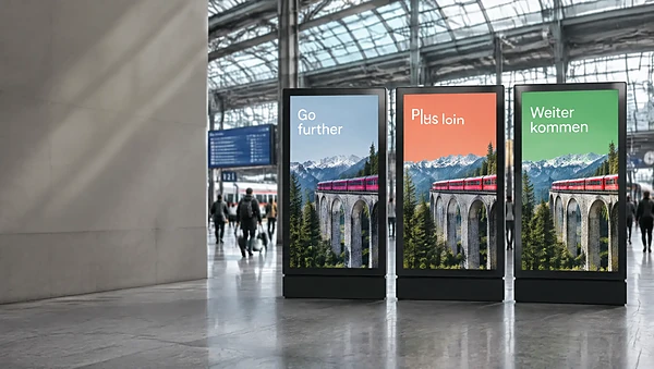 Station hall with three digital ads showing the same train campaign adapted for three languages