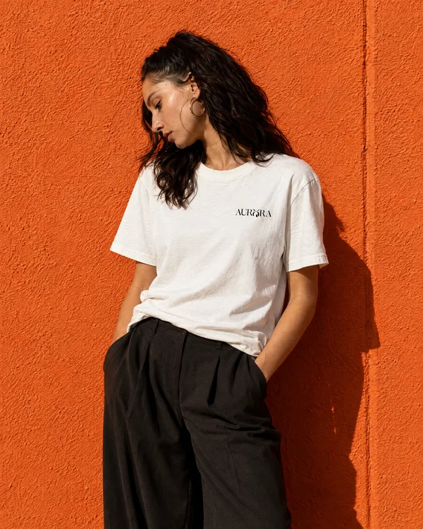 A woman in an Aurora tee against an orange wall