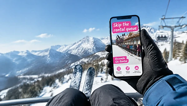 Phone on a ski chairlift showing a bold pink social ad for ski rentals