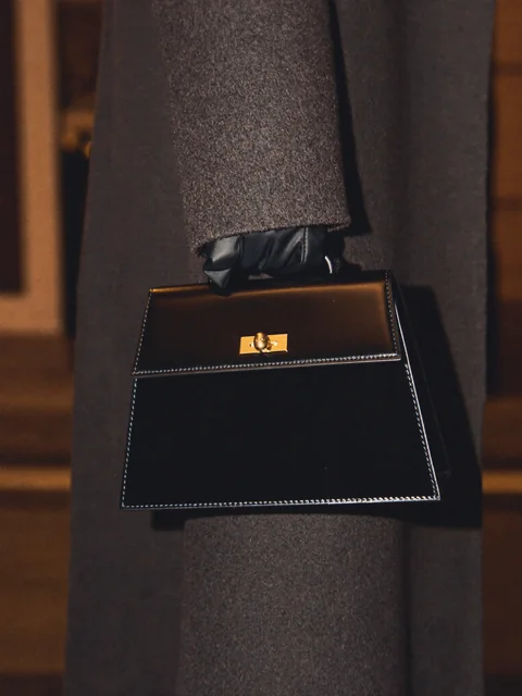 VEYRA After Dark: a gloved hand holding a black leather top-handle bag