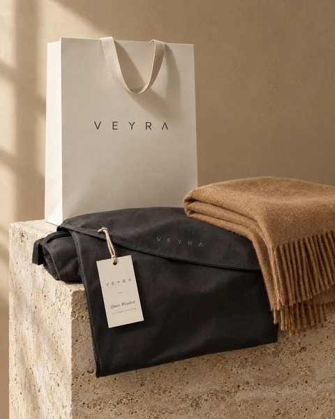 VEYRA shopping bag, garment bag and Quiet Weather hang tag on a travertine plinth